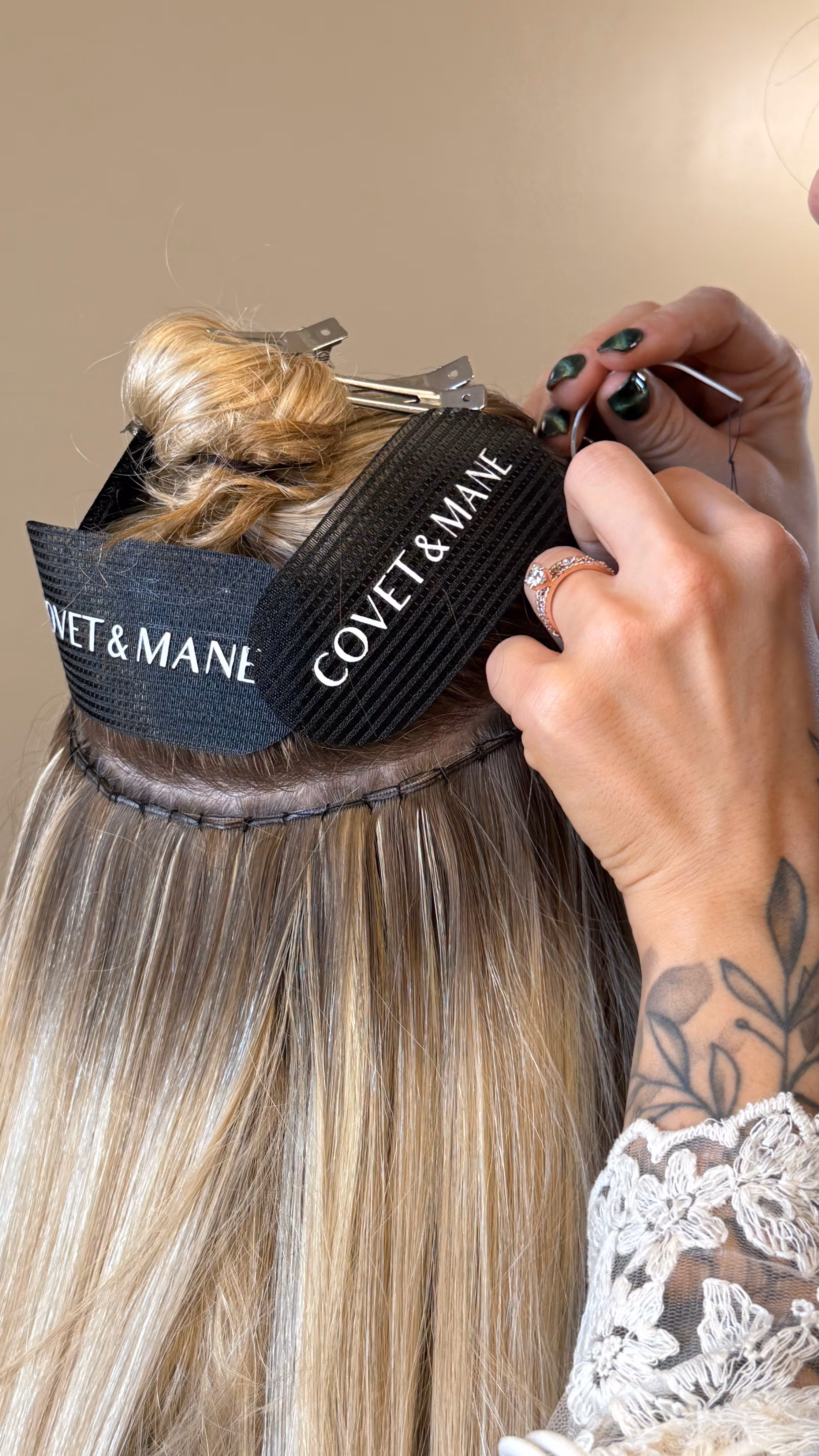 Close-up of hands sewing hair extensions to blonde hair with black Covet & Mane headbands securing upper hair.