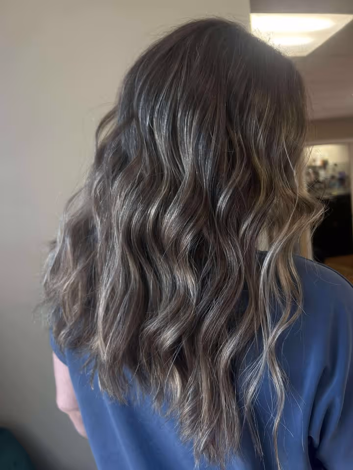 Back view of long wavy hair with frosted brown highlights on a person wearing a blue top.