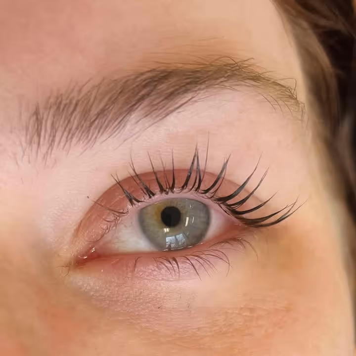 Close-up of a person's eye with long, curled upper eyelashes and light hazel iris.
