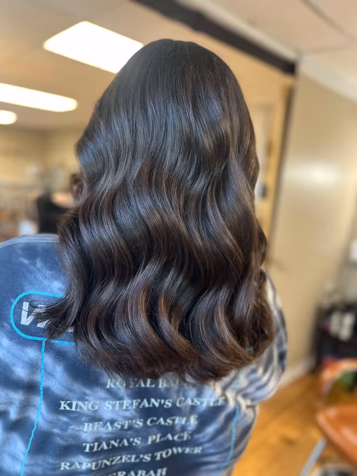Back view of a person with shiny, dark wavy hair cascading over a blue shirt with white text listing castle and tower names.