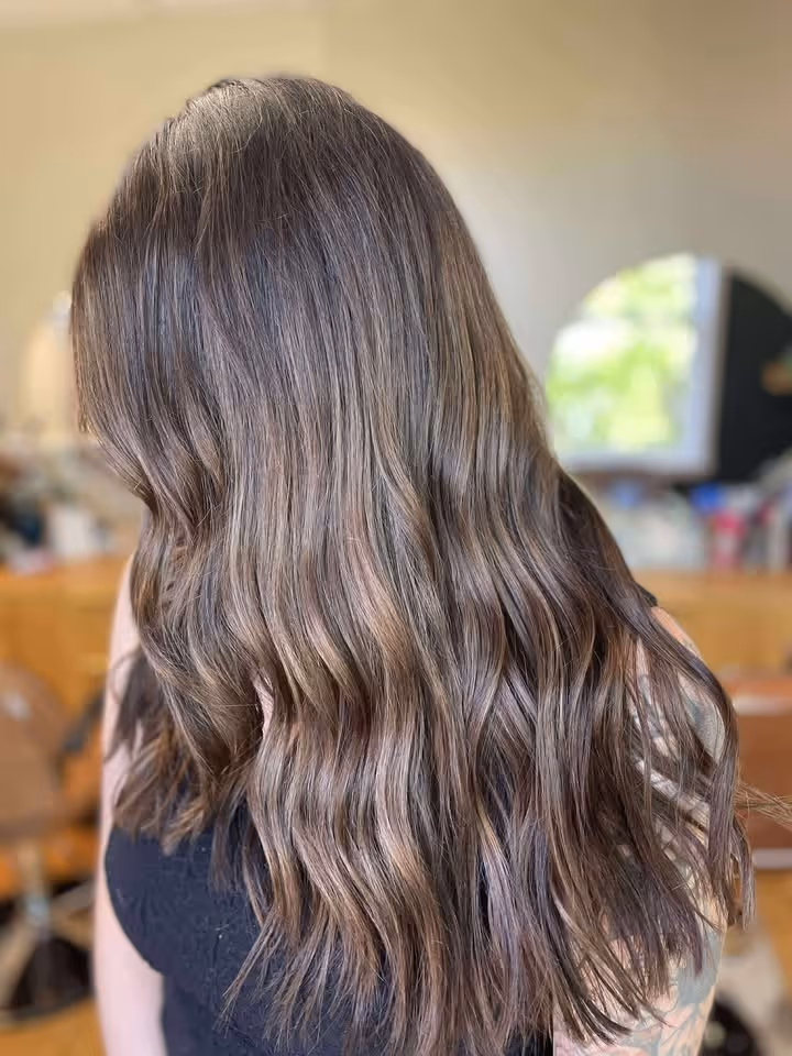 Long wavy brown hair with subtle highlights on a person wearing a black top, viewed from behind.