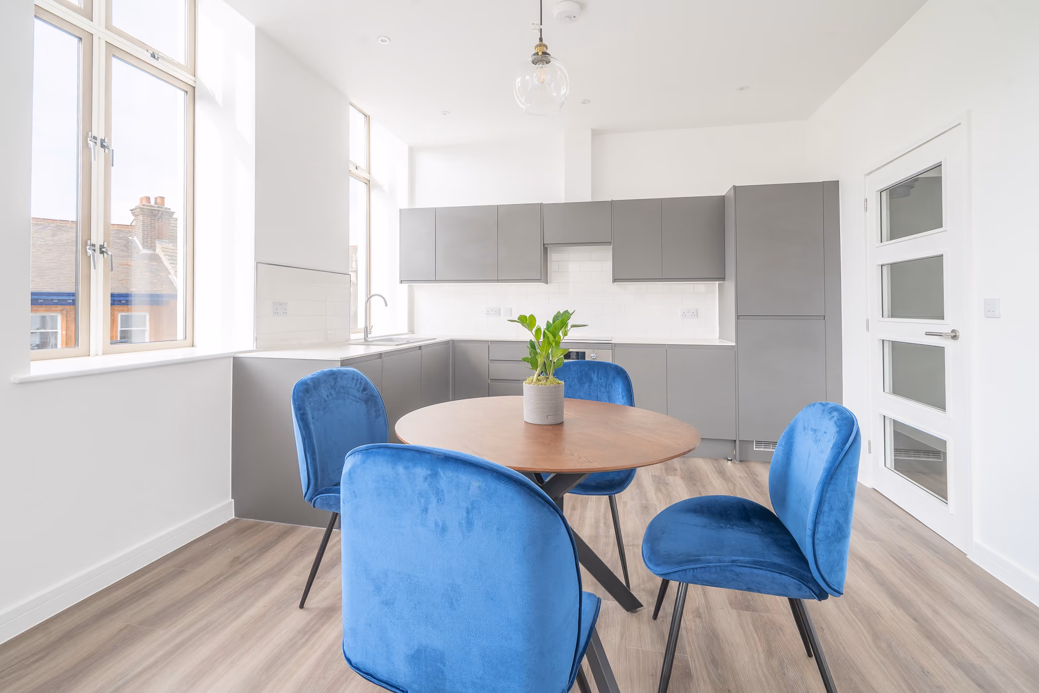 Modern kitchen with gray cabinets, round wooden table, blue chairs, and plant centerpiece.