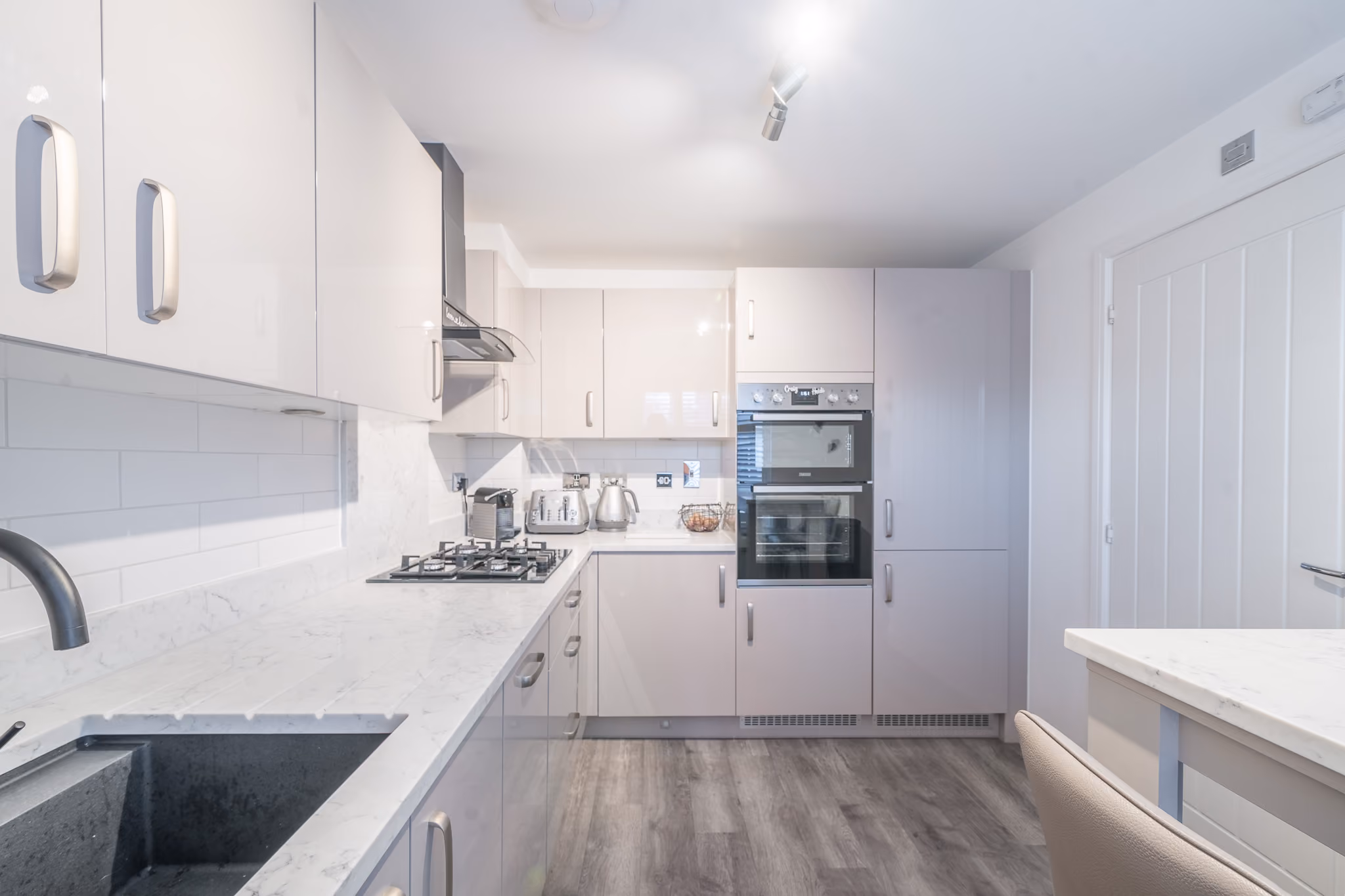 Modern kitchen with glossy cabinets, marble countertops, gas stove, double oven, and wooden floor.