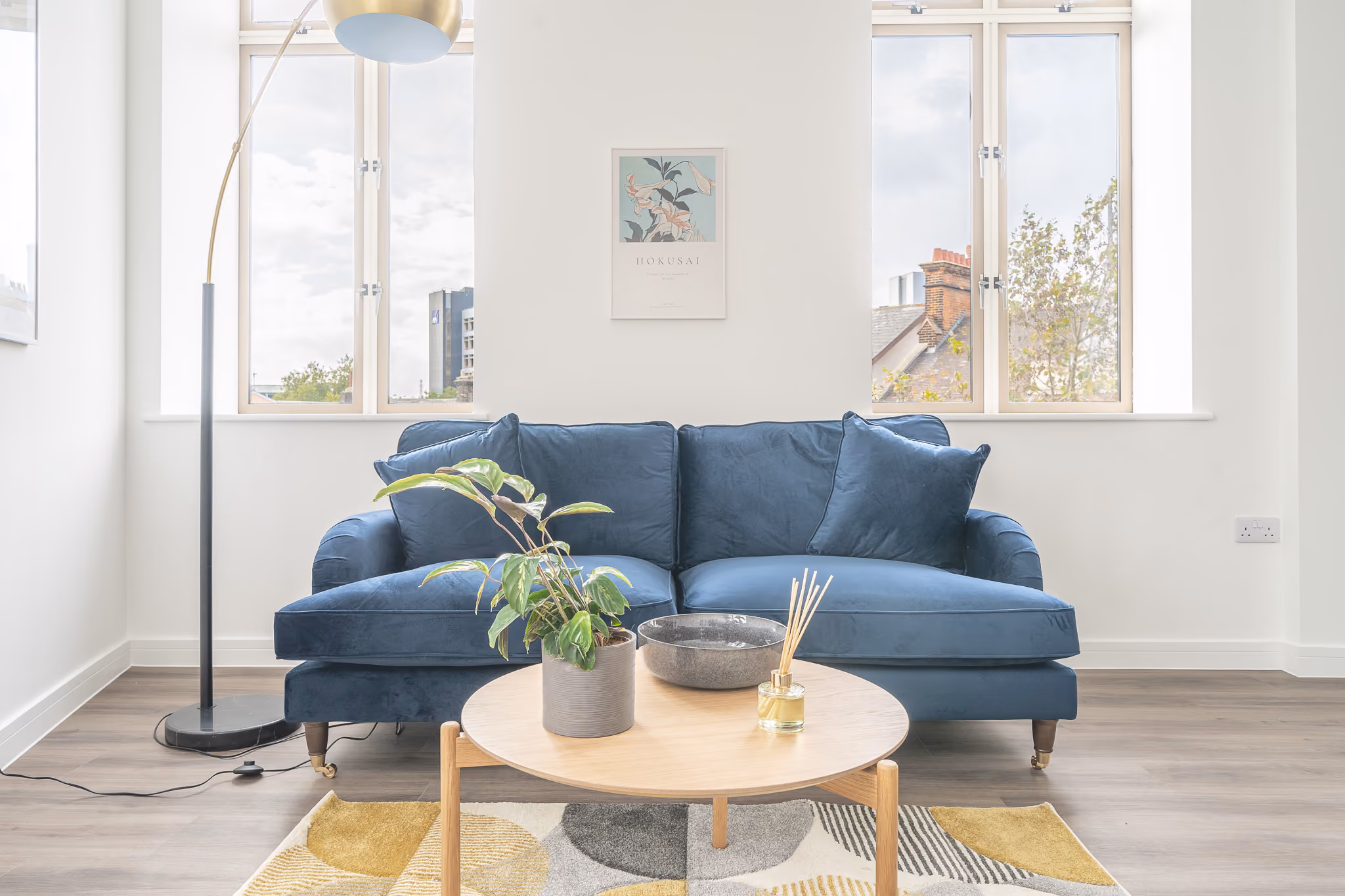Modern living room with blue velvet sofa, wooden coffee table, potted plant, and floor lamp.