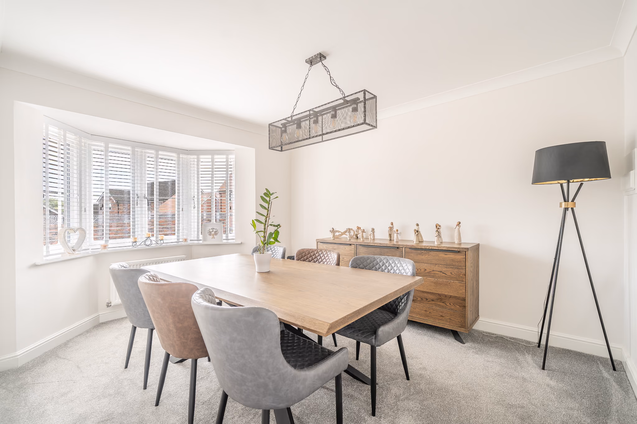 Modern dining room with wooden table, six leather chairs, sideboard with figurines, and floor lamp.