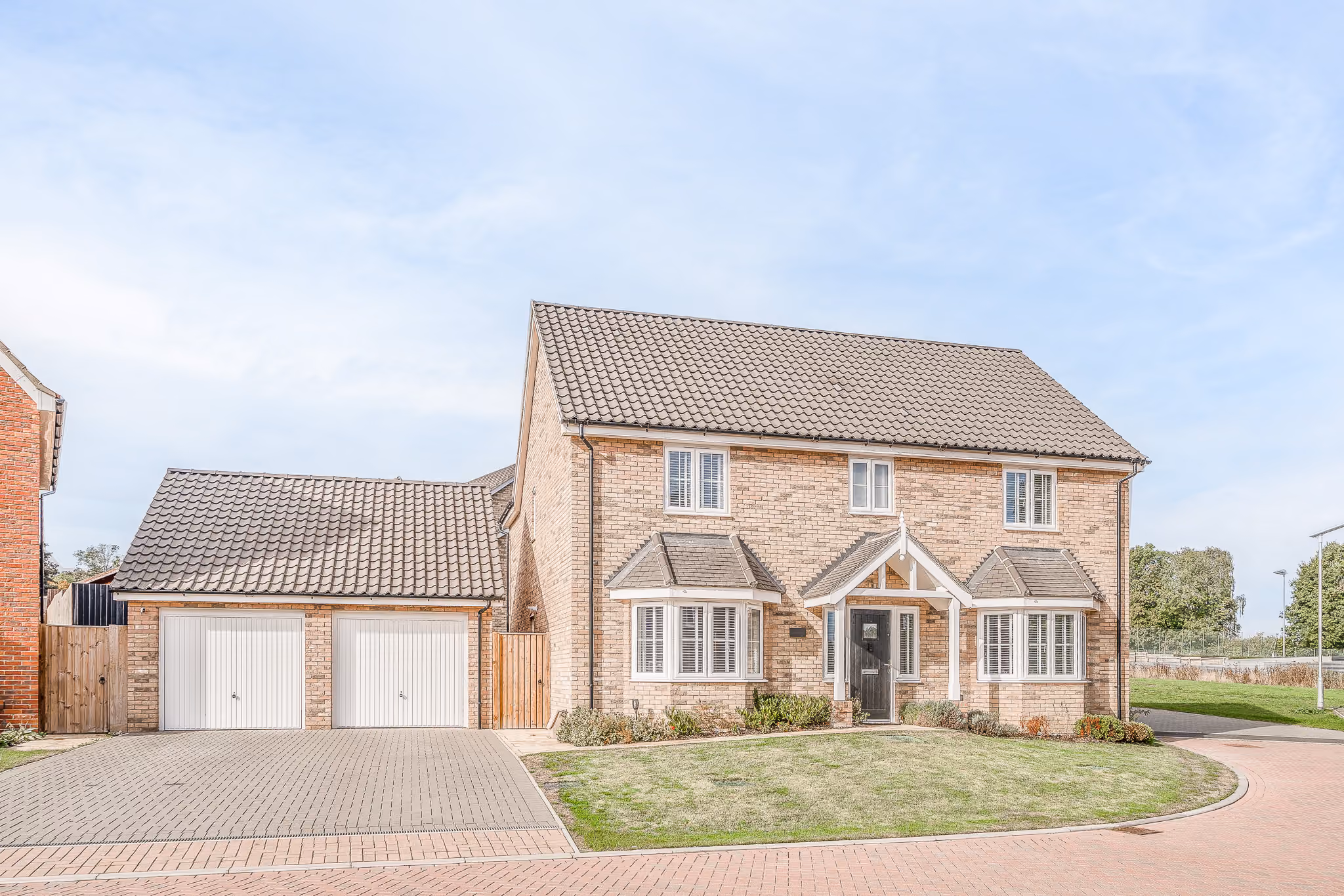 Two-story brick house with double garage, gabled roof, black front door, and small front lawn.