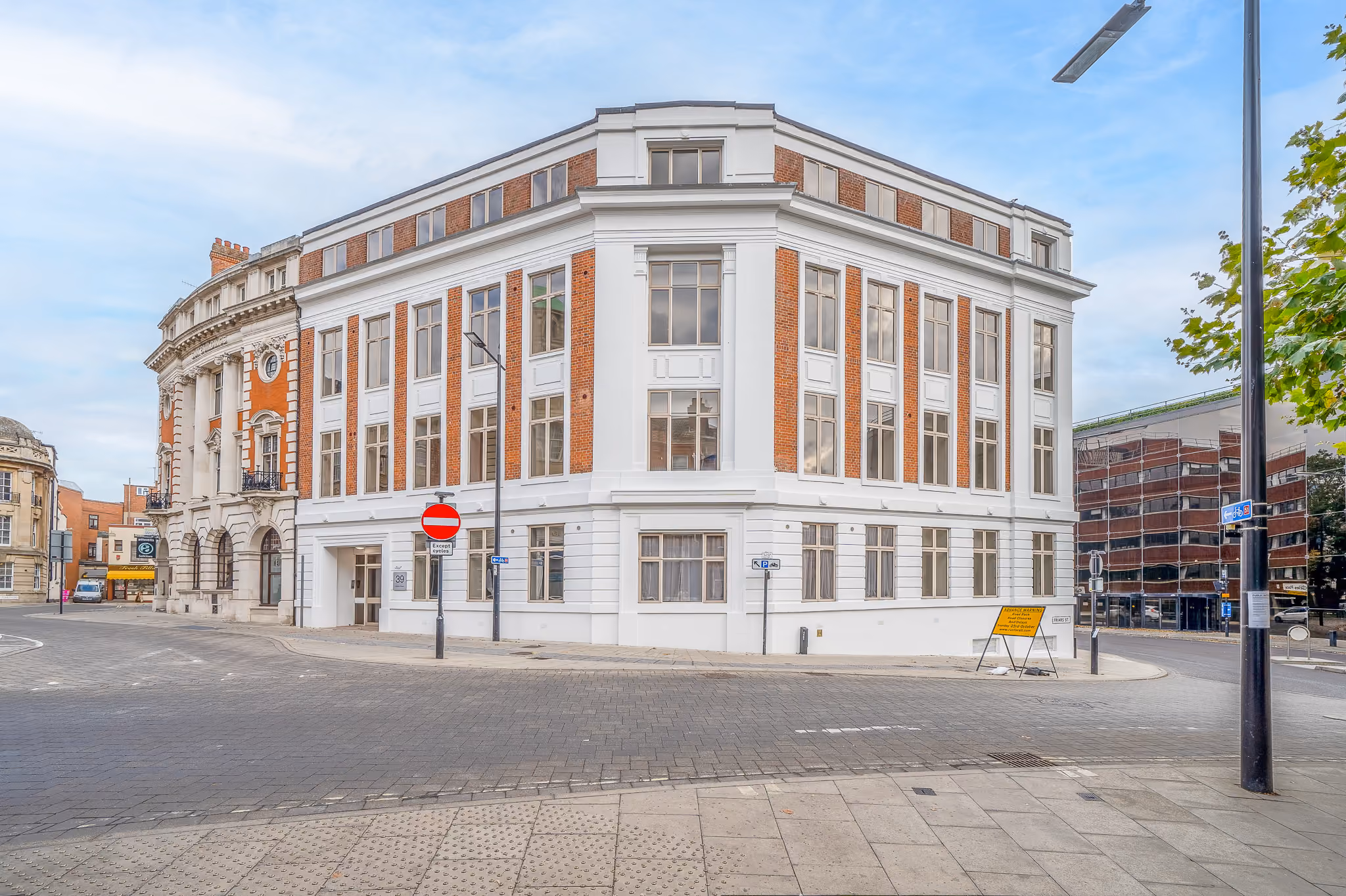 Corner view of a large white and brick building with many windows on a quiet street.