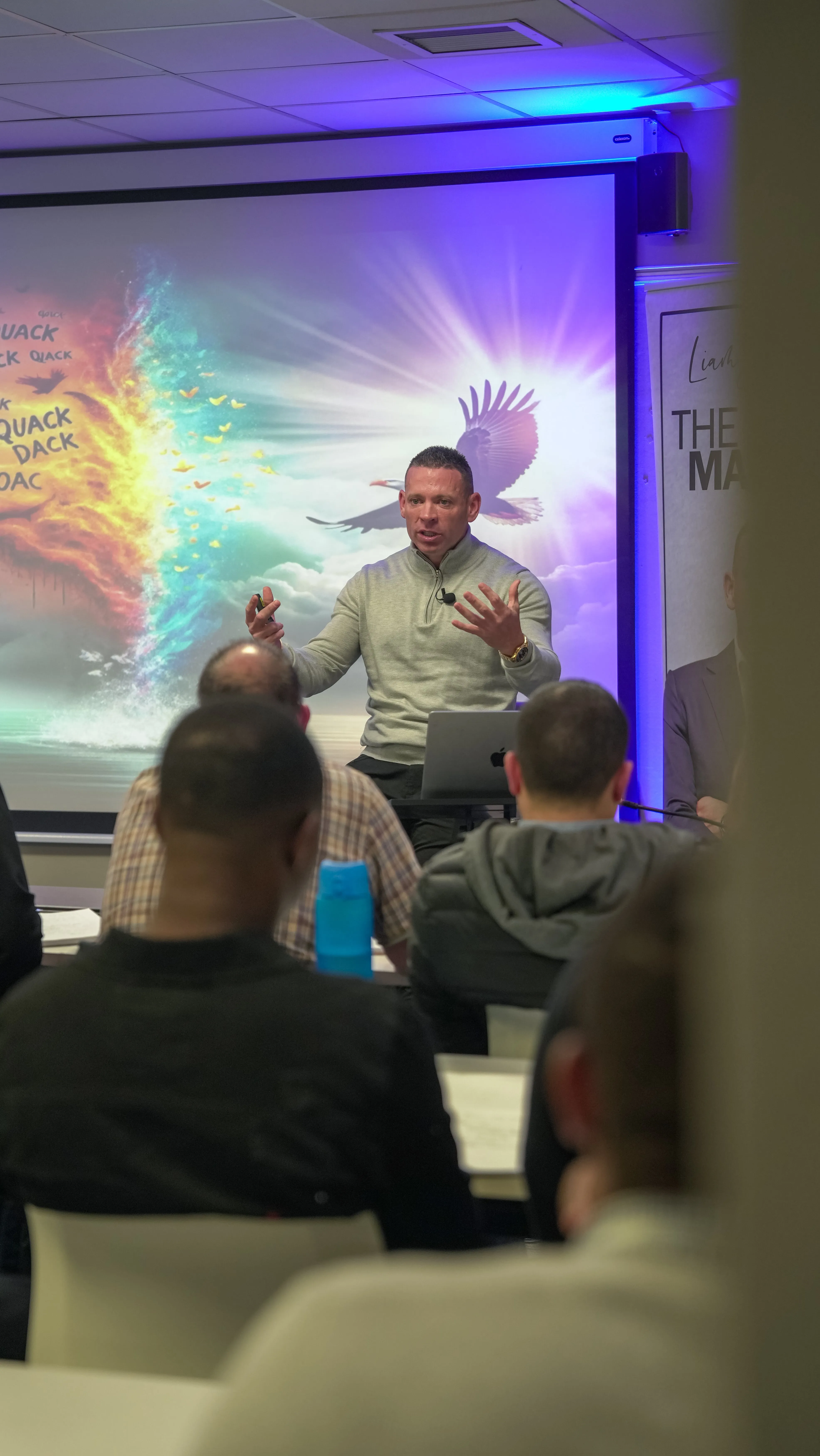 Speaker passionately presenting in front of a colorful screen with an eagle and flames to an audience.