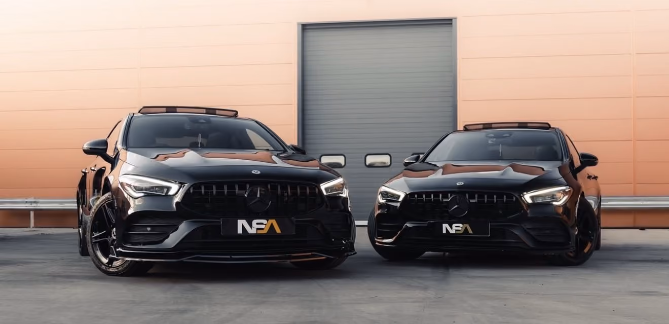 Two black Mercedes-Benz cars parked side by side in front of a large garage door.