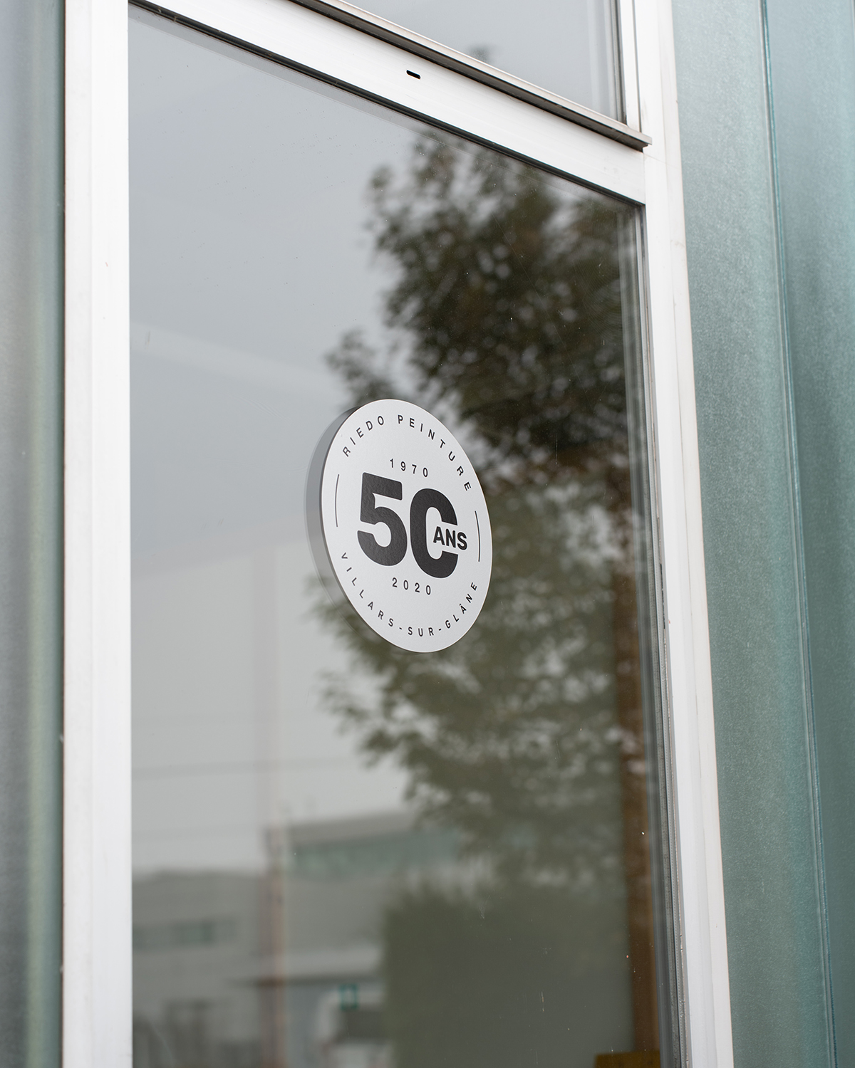 Circular white sticker on glass window commemorating 50 years of Riedo Peinture from 1970 to 2020 in Villars-sur-Glâne.