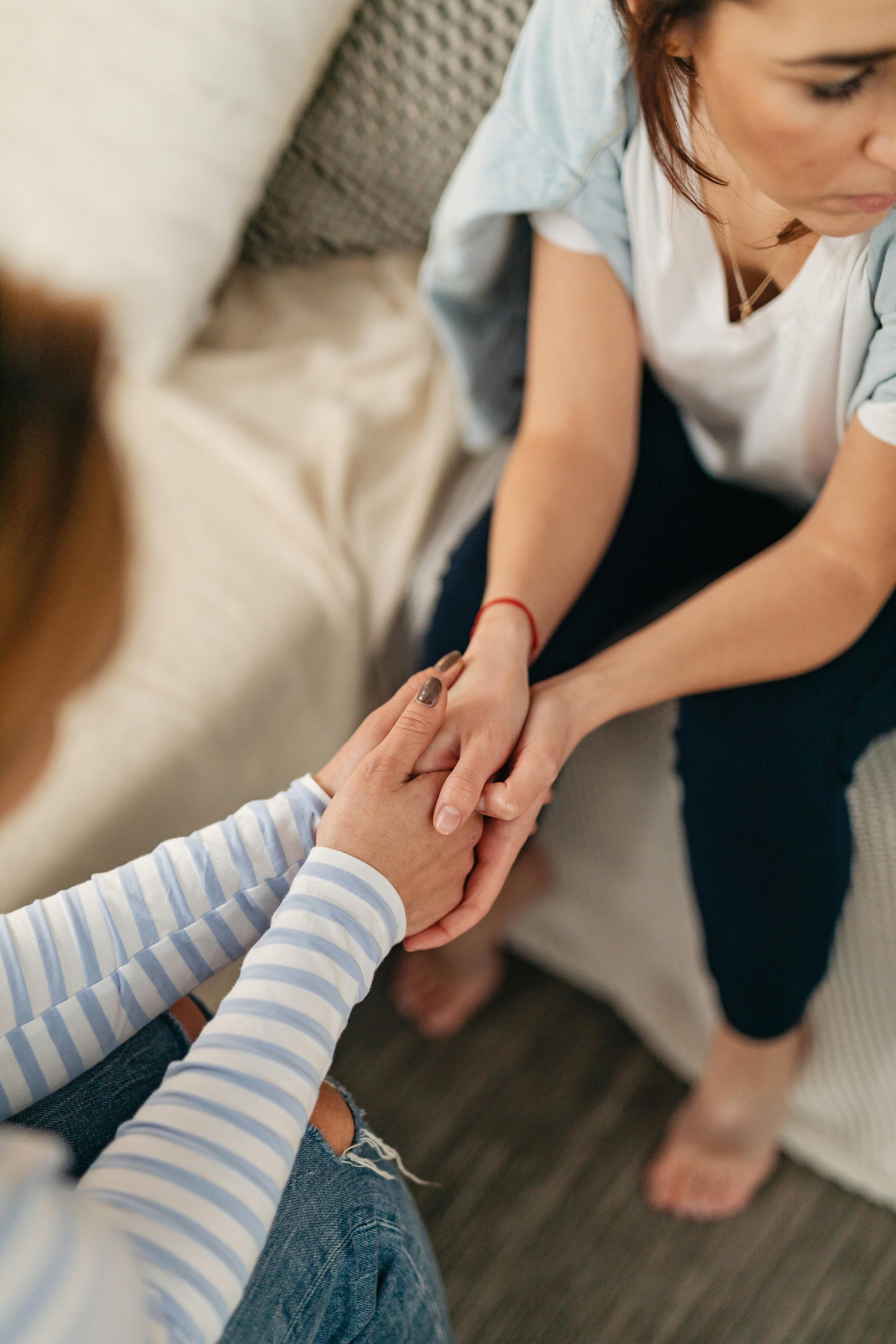 Two women sitting and holding hands in a comforting gesture.