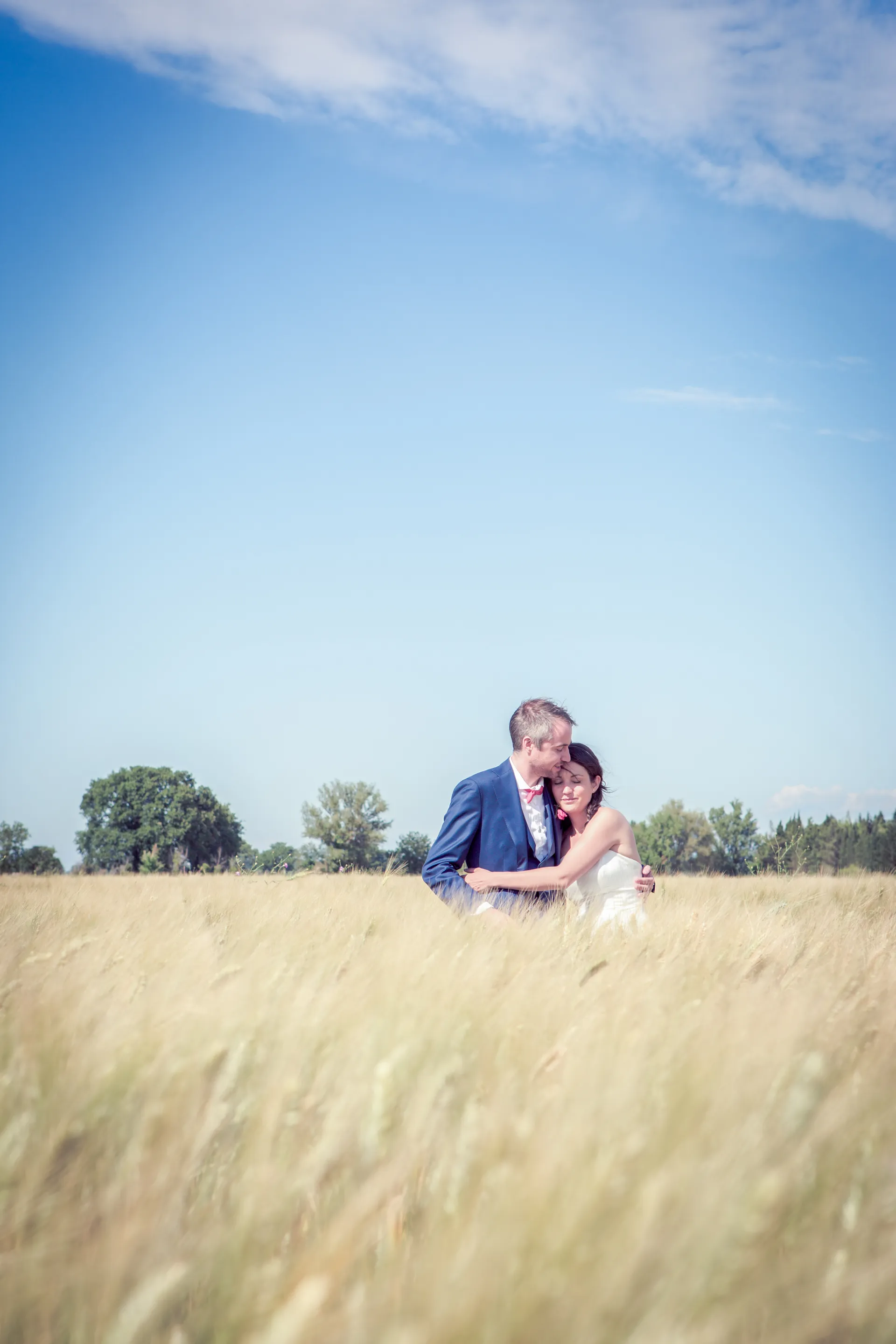 Mariés, marié anglais, enlacés face à la caméra dans les champs de blé à Arles en juin, reportage mariage élégant et naturel