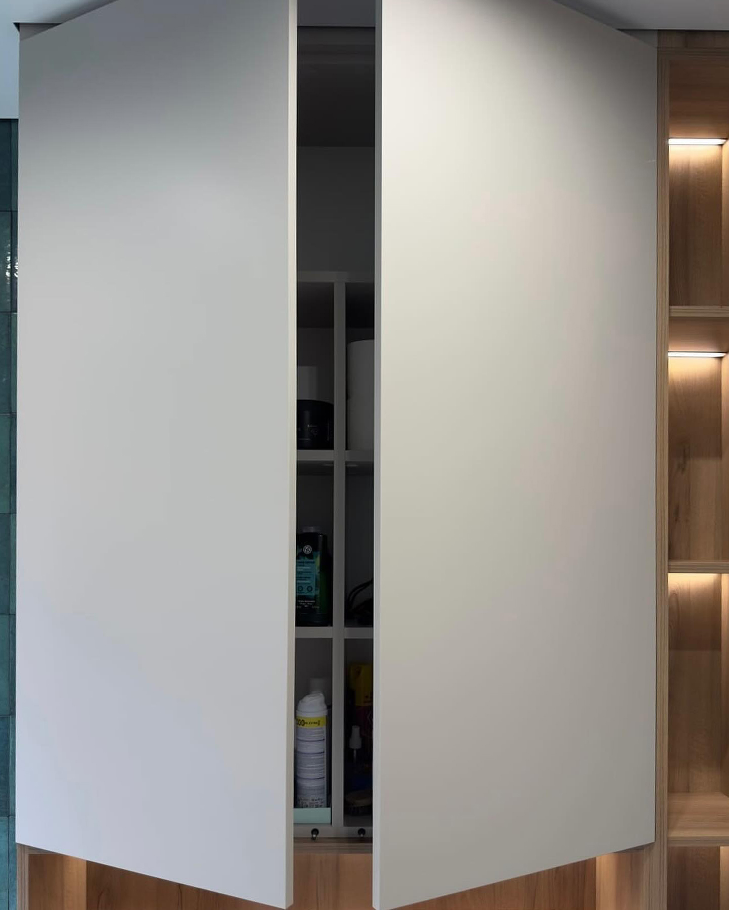 Фрагмент ванної кімнати: підвісна тумба під раковину з білими фасадами, дерев'яною стільницею та накладною білою раковиною, сіра стіна під терраццо, акцентна зелена плитка у душовій зоні.