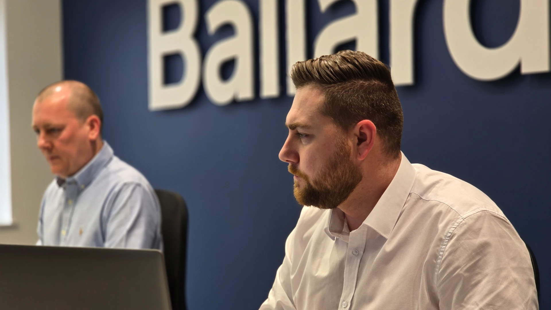 Two people having a discussion across a table in an office setting with a laptop and coffee cup on the table.