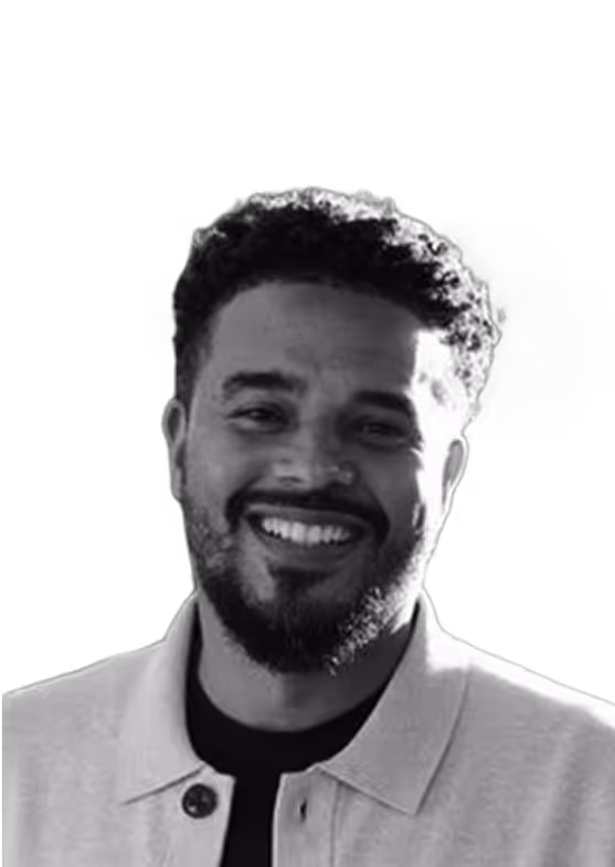 Smiling man with curly hair and beard wearing a light-colored jacket over a dark shirt.