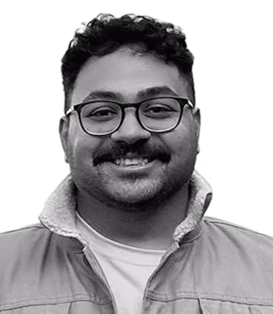 Smiling man with curly hair, glasses, and a mustache wearing a jacket over a shirt.