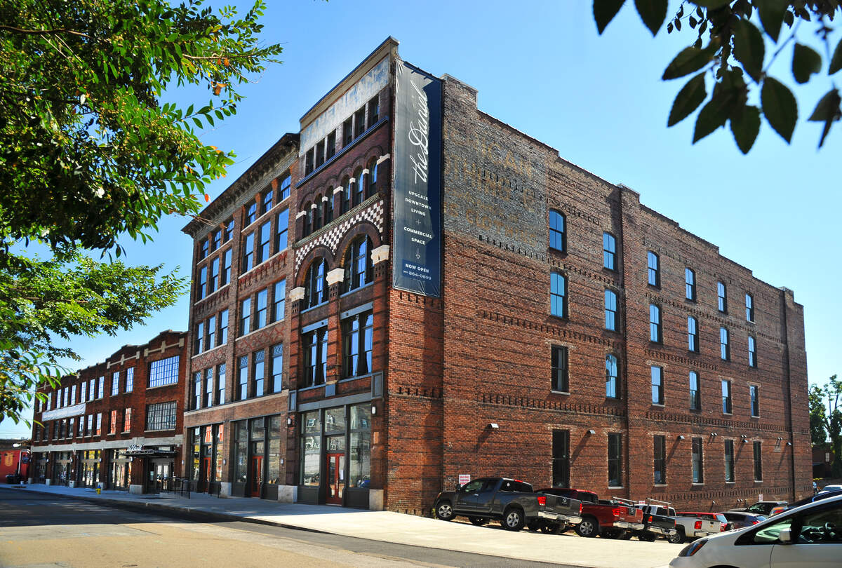 Brick commercial building with large windows and a banner reading 'The Denizen' on a sunny day with parked cars.