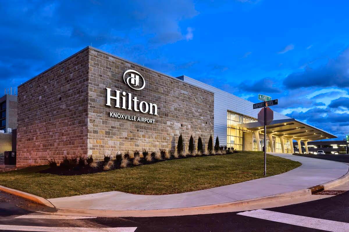 Hilton Knoxville Airport hotel building exterior at dusk with illuminated sign and modern entrance canopy.