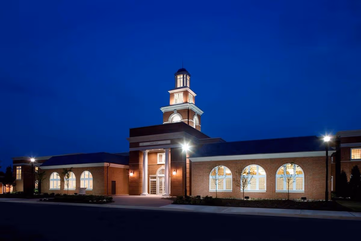 Illuminated brick building with white columns and arched windows at night under a deep blue sky.