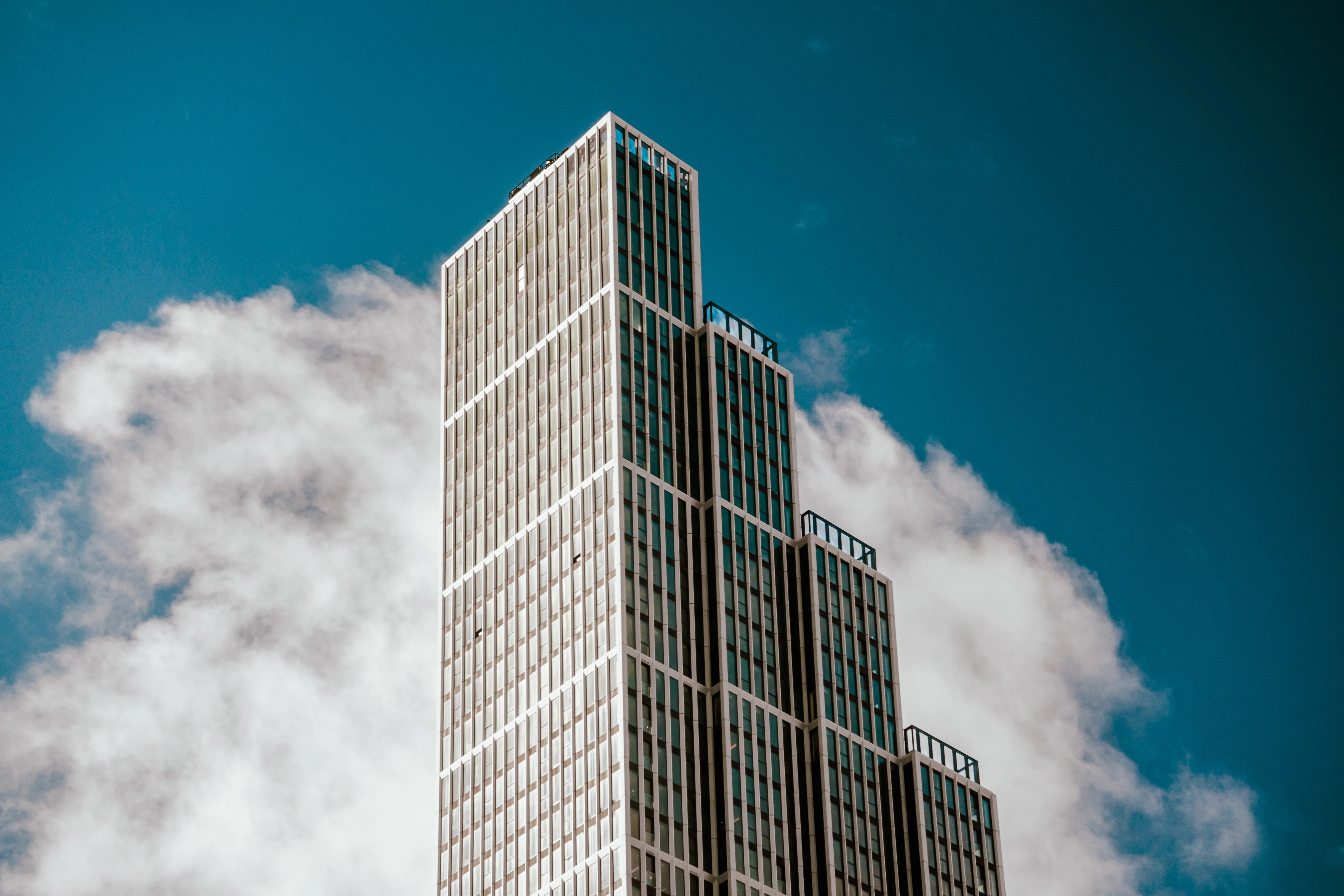 Modern stepped skyscraper with glass windows against a blue sky with white clouds.