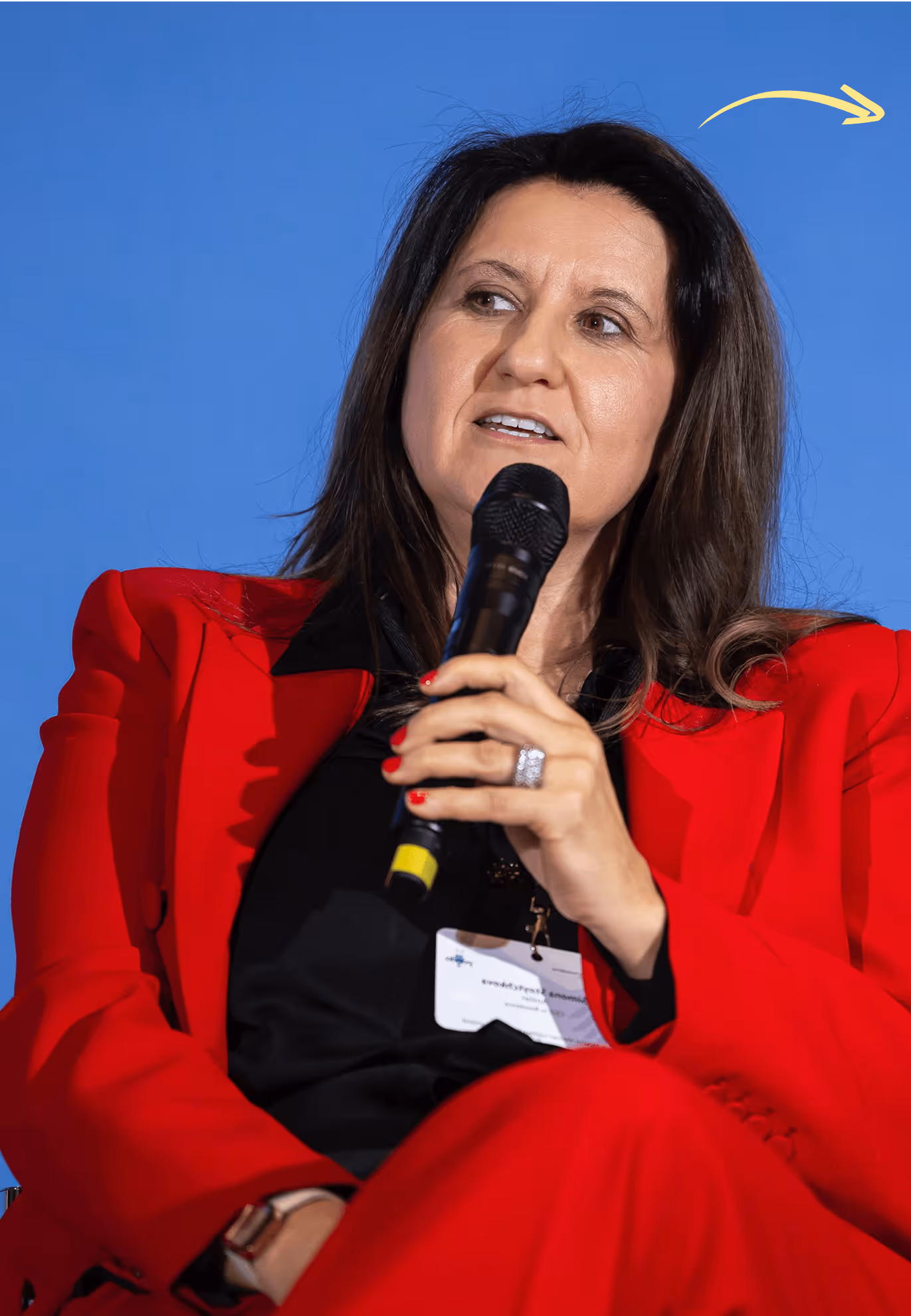Frau in rotem Anzug spricht in Mikrofon vor blauem Hintergrund.