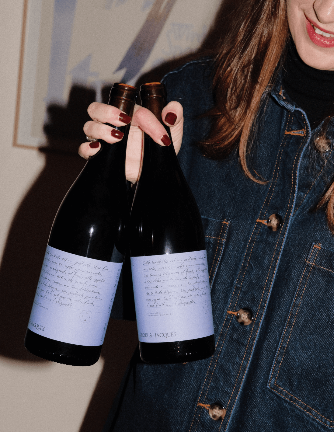 A photograph of a woman showing two label design of bottles of Pinot Noir red wine for Domaine Croix Saint Jacques, French Wine Producer