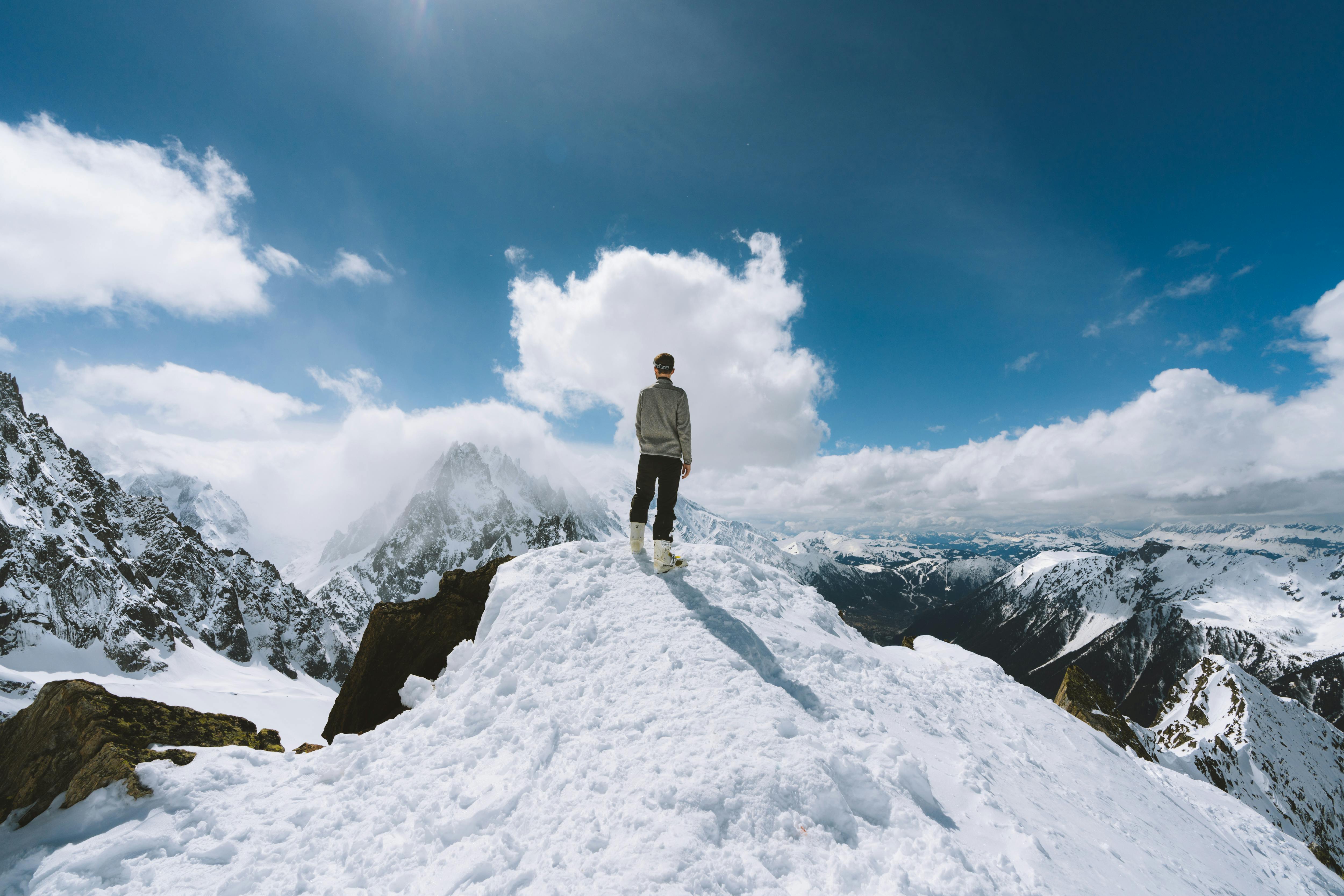 Homme debout au sommet d’une montagne enneigée avec vue panoramique.