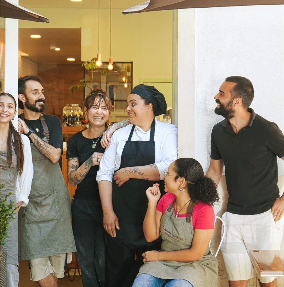 Equipa de restaurante sorrindo e interagindo alegremente em frente à entrada do estabelecimento.