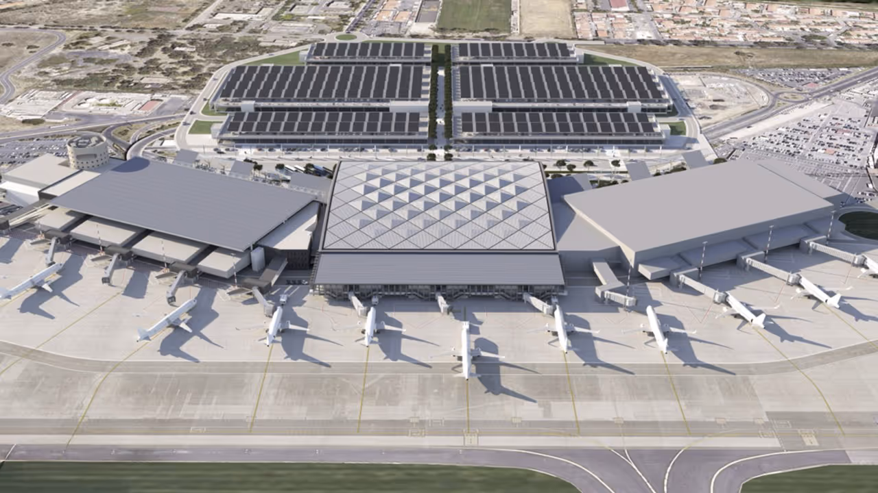 Aerial view of an airport terminal with multiple airplanes parked at gates and large solar-panel-covered buildings behind it.