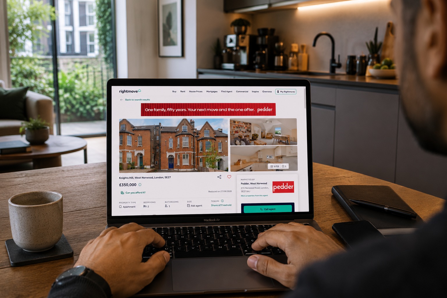 Male property investor browsing a reduced South London flat listing on a MacBook in a modern kitchen.
