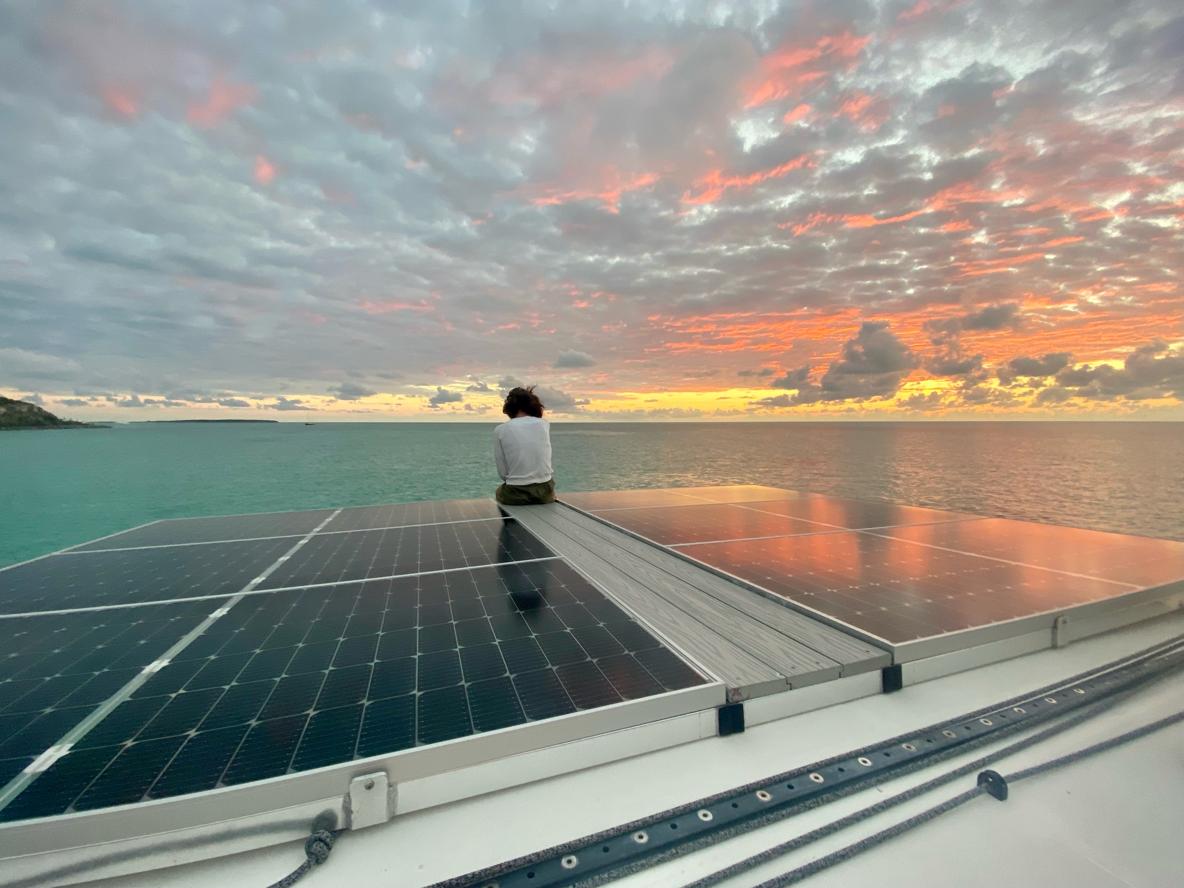 Person sitting on a solar panel near the ocean watching the sunset.