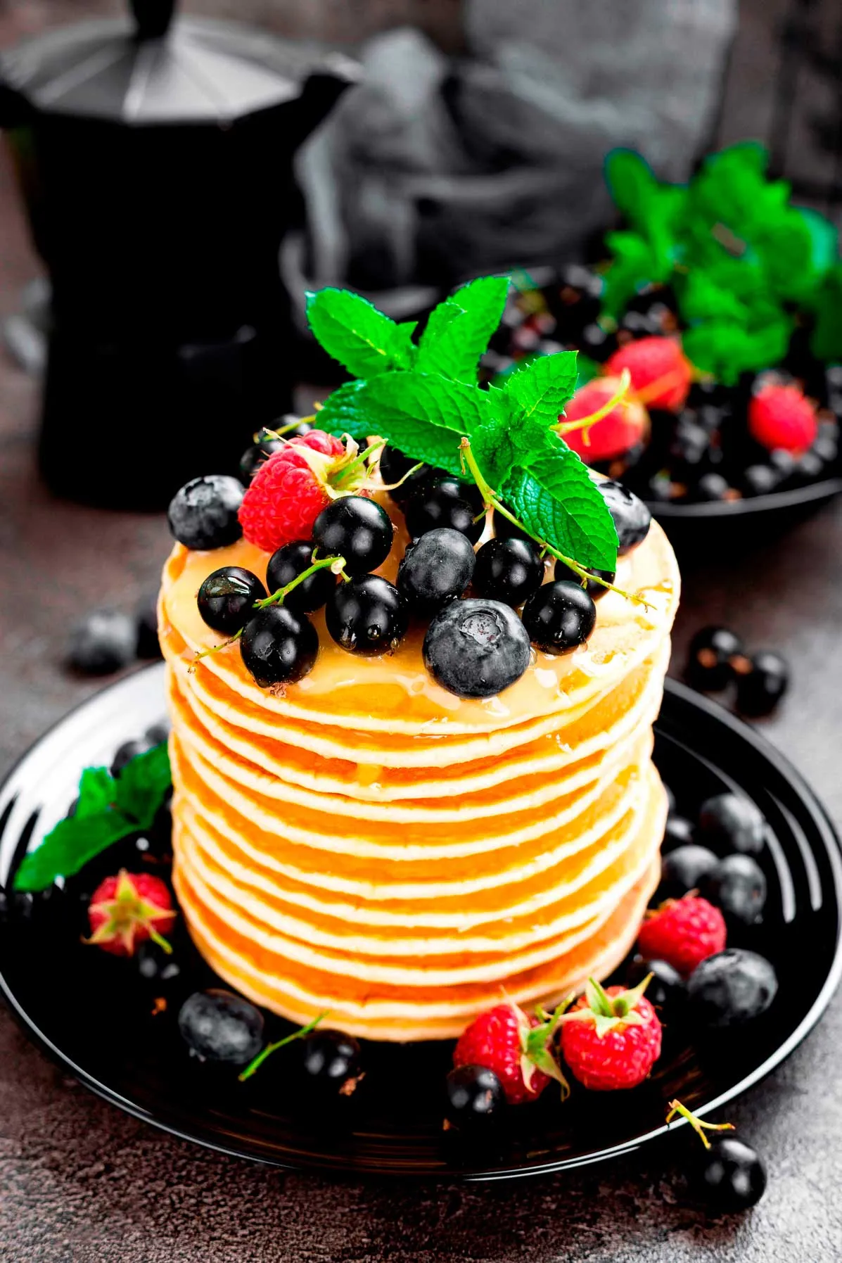 A stack of fluffy pancakes topped with fresh berries and mint leaves, served on a white plate.