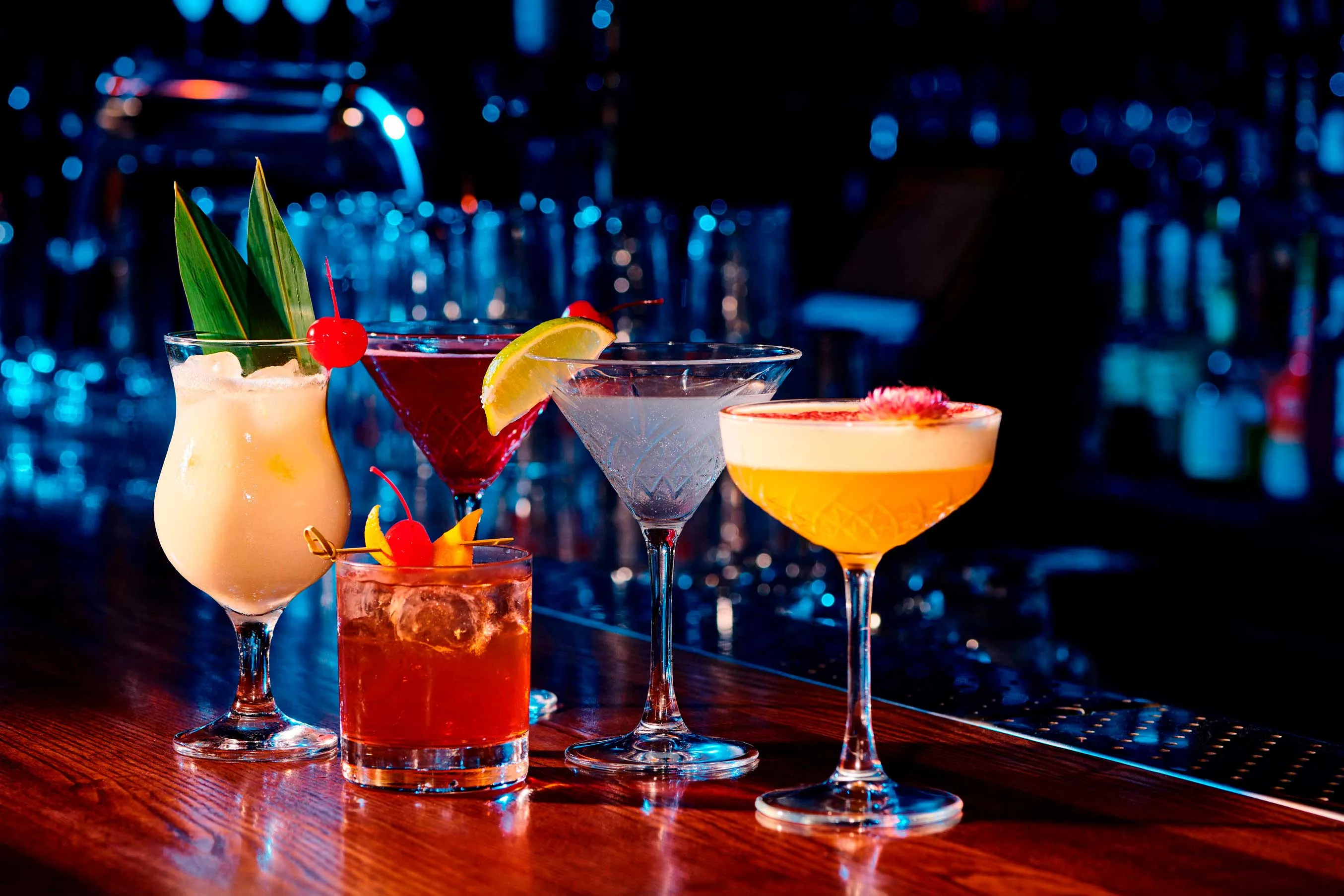  A variety of colorful cocktails arranged on a polished bar, showcasing different garnishes and glassware.