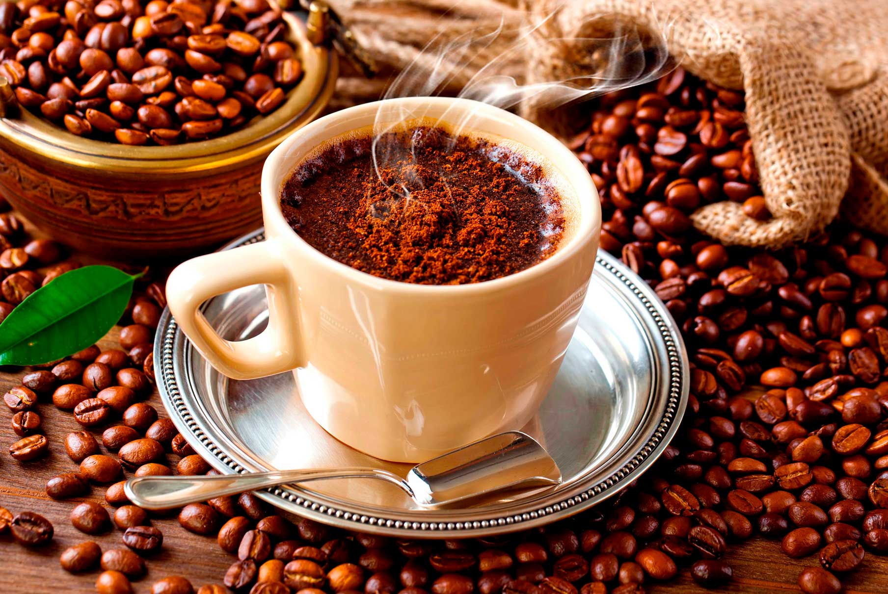 A cup of coffee surrounded by scattered coffee beans on a wooden surface.
