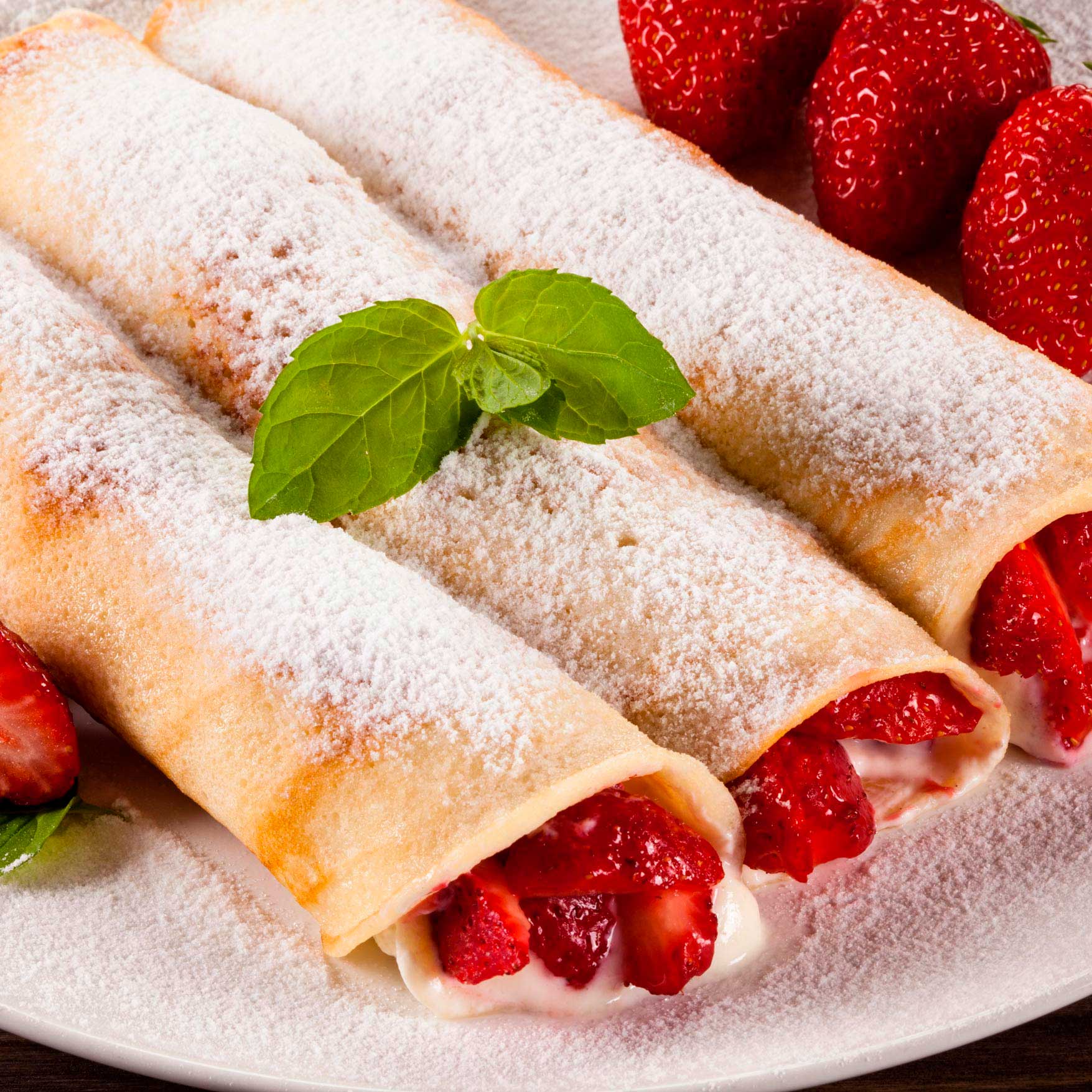 A plate of delicate crepes garnished with fresh strawberries, showcasing a delightful and colorful dessert presentation.
