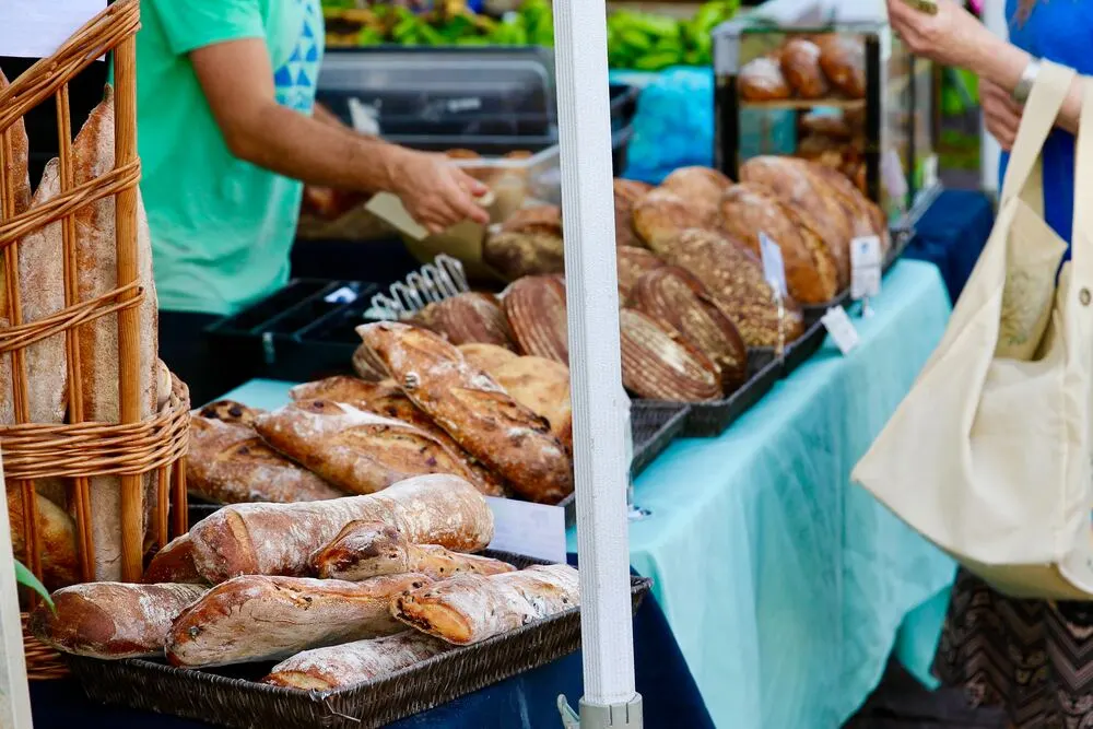 People trying samples of fresh baked bread loaves at farmers market table