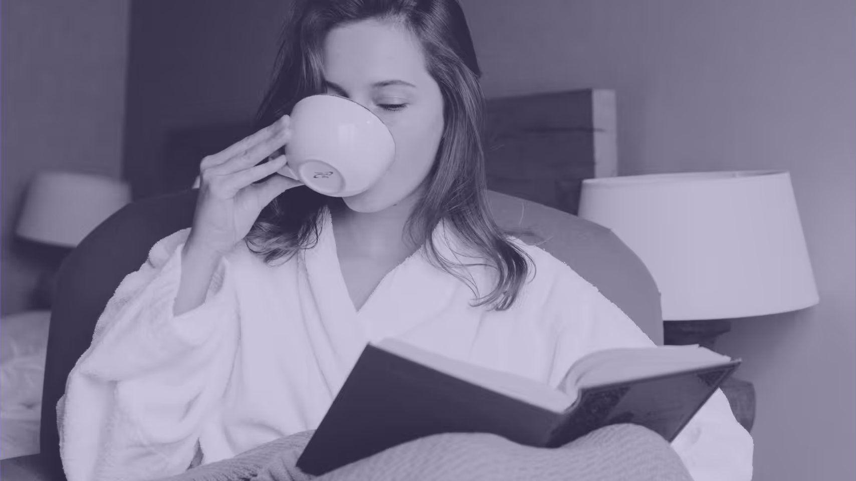A person in a robe drinking a cup of coffee while reading a book