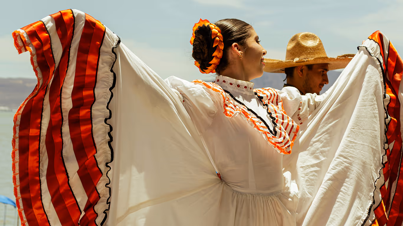 Woman in traditional Mexican dress with red and white stripes dancing next to a man wearing a straw sombrero hat.