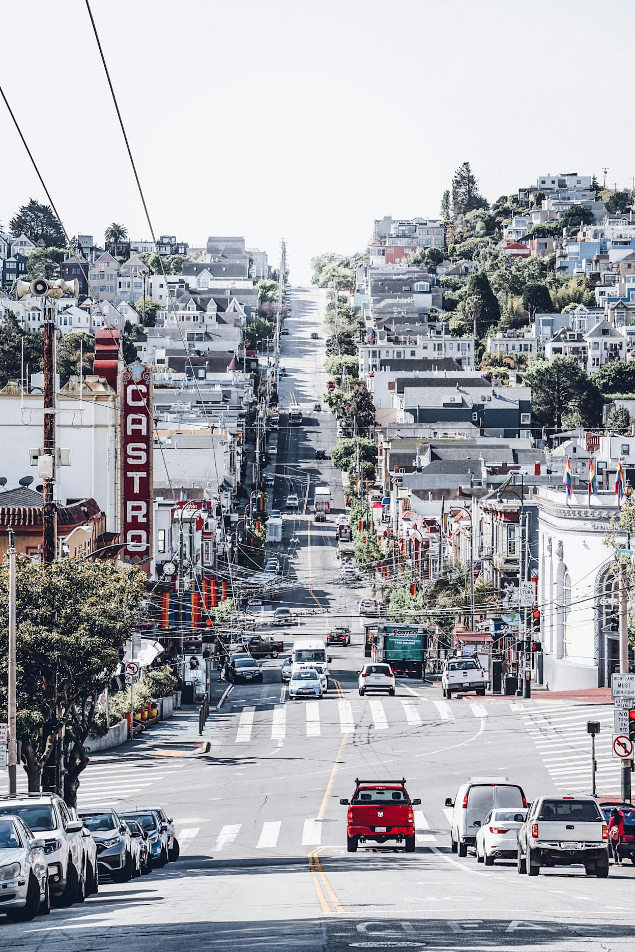 Taken in the middle of a street in the Castro neighborhood in San Francisco. On the next block, the road goes up a hill lined with houses. In the foreground, you can see a vertical theatre sign spelling out "CASTRO"
