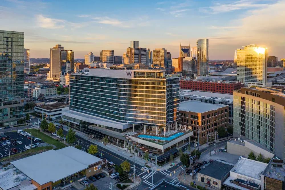 An aerial image of the W Hotel Nashville in The Gulch neighborhood. Among other tall and modern buildings, the W has a rooftop pool and glass walls that look out at the surrounding city. The downtown skyline is visible in the background.