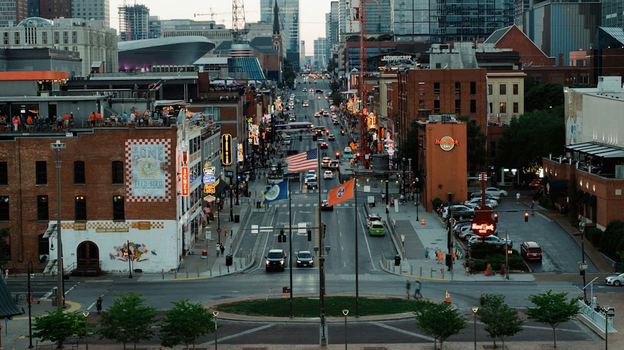 An image taken from a high building in Downtown Nashville of Broadway Street, a popular nightlife hub in the area. The street is lined with bars and storefronts, and there are many cars driving along the road.