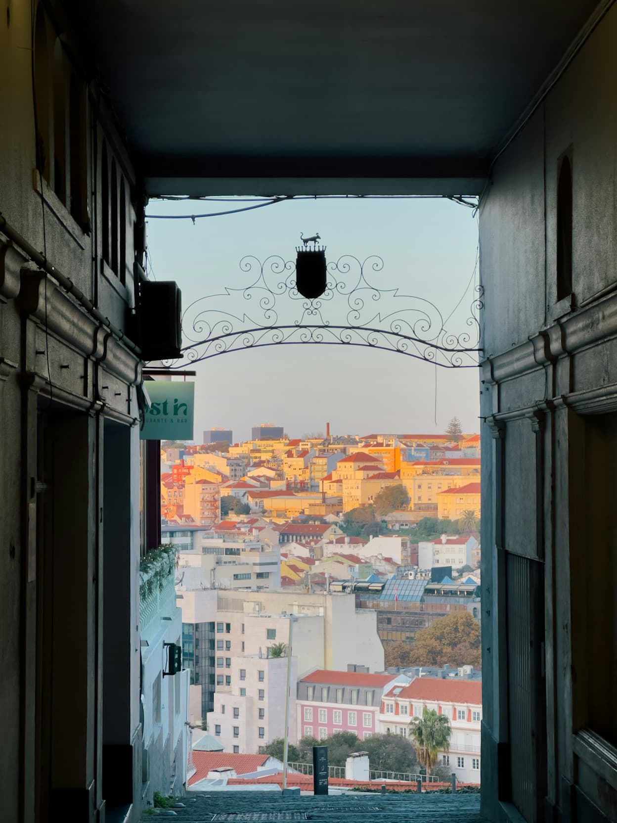 An image was through a window in the Príncipe Real neighborhood in Lisbon. Sunset glow shines across the city, and from the hilltop perspective, you can see the sprawling white buildings with terracotta roofs.