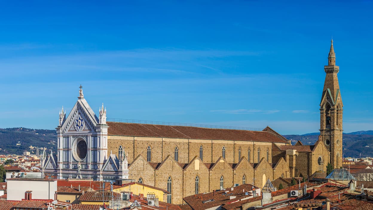 An image of the famous church in the Santa Croce neighborhood in Florence, Italy. The church protrudes from the rest of the city's skyline, and goes above even the mountains in the horizon of the image. 