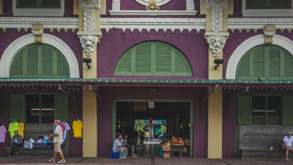 An image taken across the street from La Placita de Santurce, a popular farmers market in San Juan. The exterior is painted purple, yellow, and green, and people sit and stand outside and inside at various stands.
