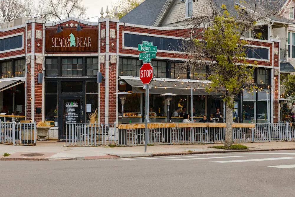 An image of a restaurant storefront in the Highlands neighborhood in Denver, Colorado. The restaurant has some outdoor tables and takes up a corner lot.  