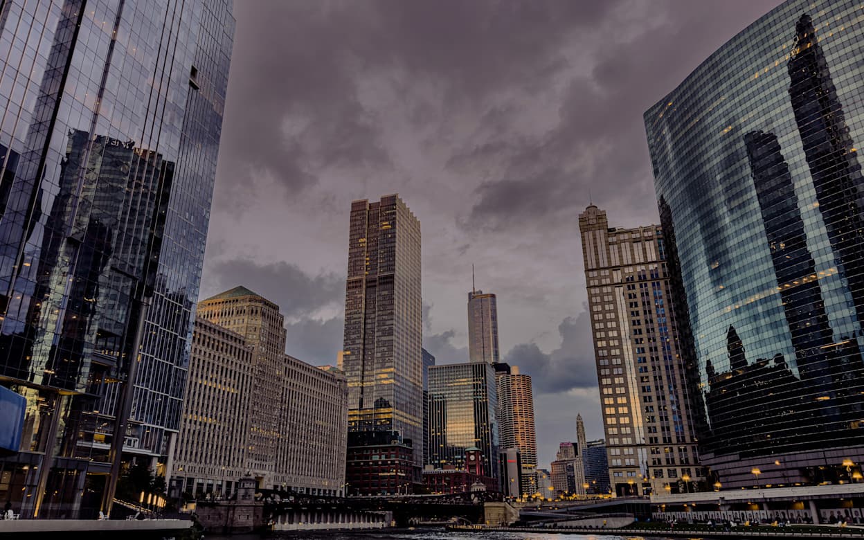 The tall skyscrapers in the River North neighborhood in Downtown Chicago. Taken at night, the dark sky is cloudy and the buildings reflect off of each other and lit up from indoor lights.