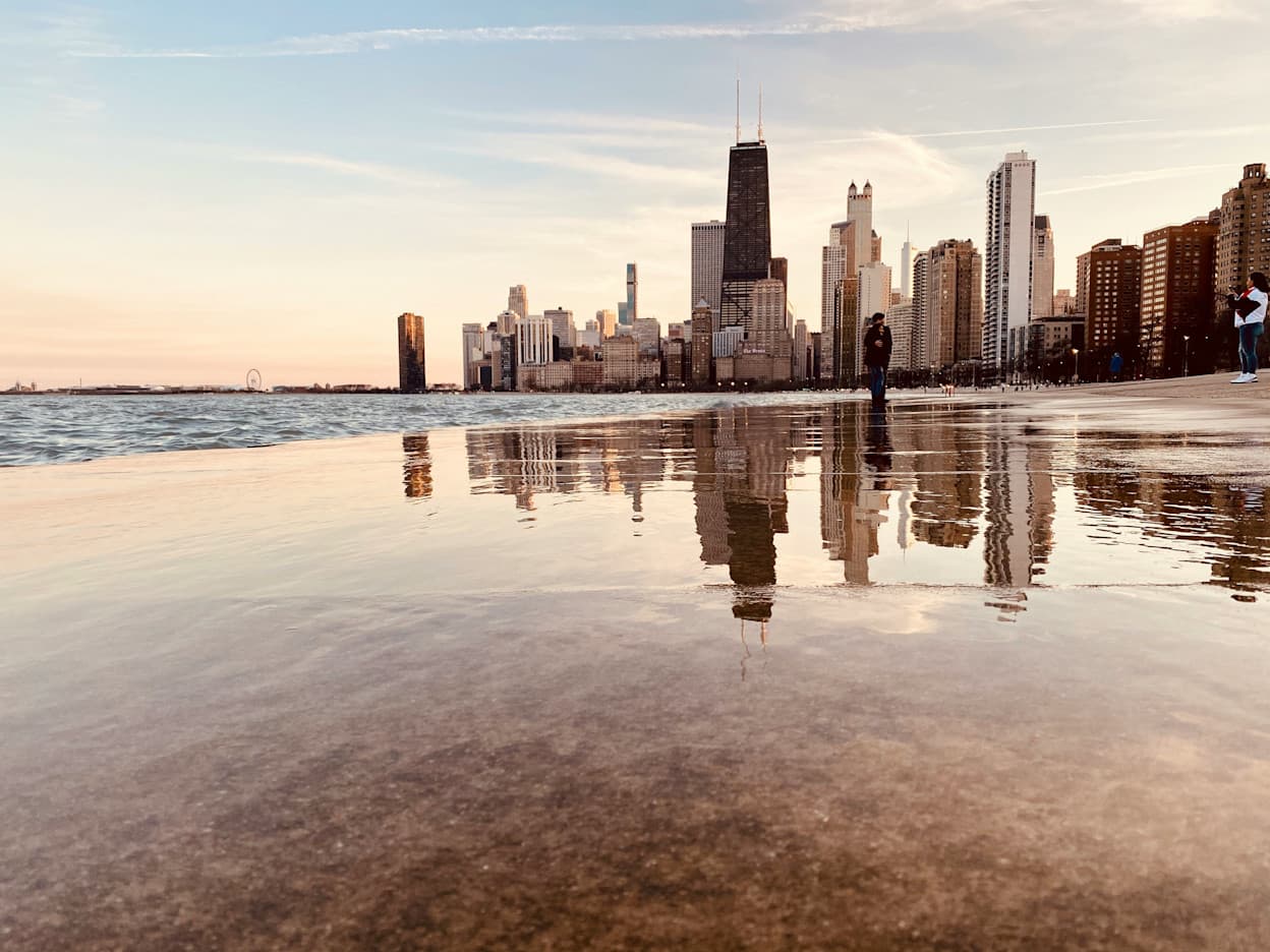Taken along a body of water in Lincoln Park, Chicago. The city skyline reflects on the water, and the sky is orange at sunset which also reflects in the water.