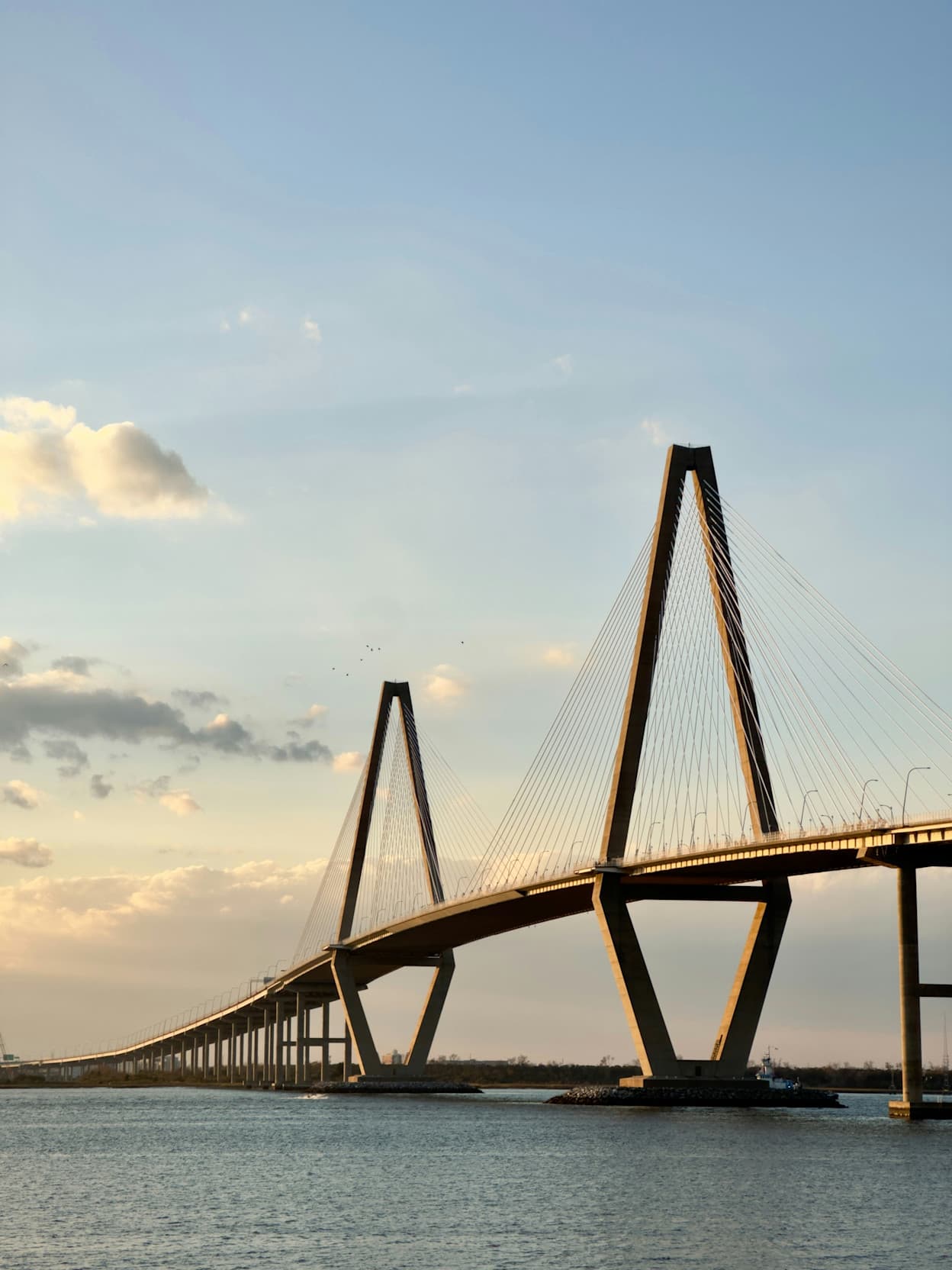 The large bridge connecting Downtown Charleston to the Mount Pleasant area, in South Carolina. The bridge continues into the distance, and the highest points have large pillars going hundreds of feet above the driving level of the bridge.