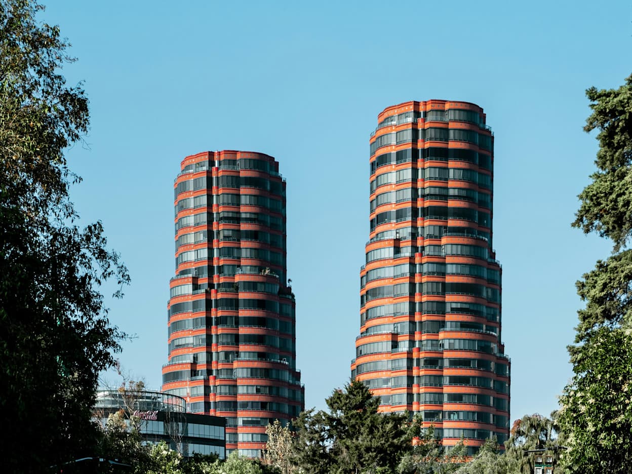 Two skyscrapers with colorful details shoot above the trees in a park, creating a mini-skyline view in the Polanco neighborhood of Mexico City.