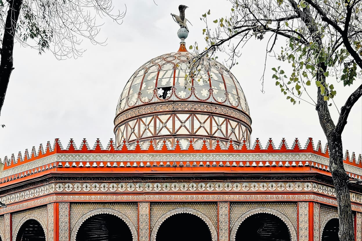 A historic carousel for children, painted in ornate red detail, sits in a park in the Santa María La Ribera and the San Rafael neighborhoods of Mexico City. 